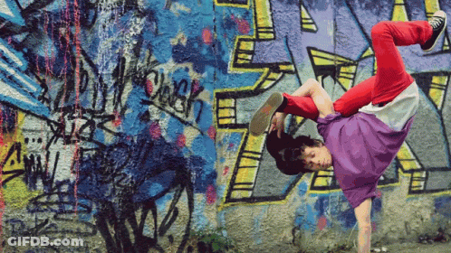 A Person Is Doing A Handstand In Front Of A Wall With Graffiti On It Including The Letter R GIF