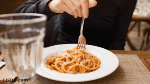 A Person Is Eating Spaghetti With A Fork In Front Of A Glass GIF