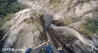 A Person Is Flying Over A Waterfall In The Mountains . GIF