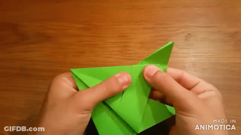 A Person Is Folding A Green Origami Piece On A Wooden Table GIF