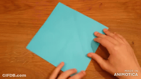A Person Is Folding A Piece Of Blue Paper On A Wooden Table . GIF