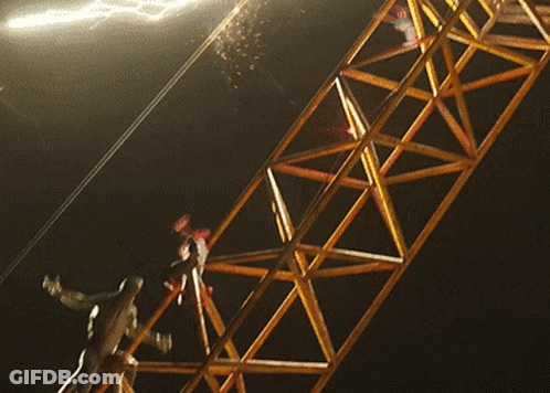 A Person Is Hanging From A Metal Structure With A Light Behind Them GIF