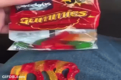 A Person Is Holding A Bag Of Gummy Worms On Their Lap . GIF