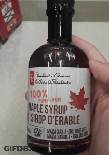 A Person Is Holding A Bottle Of Maple Syrup In Their Hand GIF