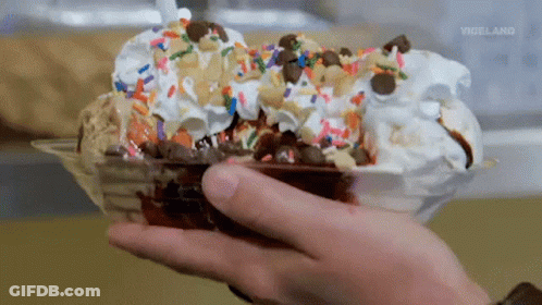 A Person Is Holding A Bowl Of Ice Cream With Chocolate Sauce And Sprinkles .. GIF