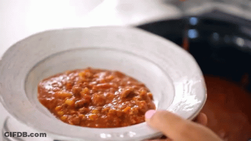 A Person Is Holding A Bowl Of Tomato Sauce In Front Of A Pot Of Sauce . GIF