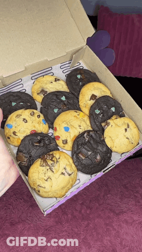 A Person Is Holding A Box Of Cookies With Different Flavors On Them GIF