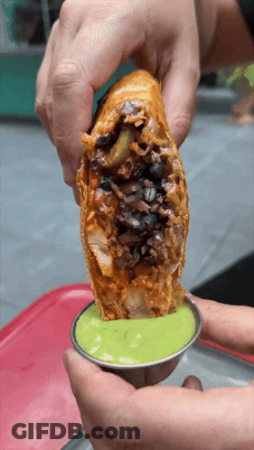 A Person Is Holding A Burrito In Their Hands And Dipping It In Green Sauce GIF