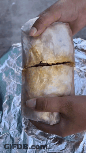 A Person Is Holding A Burrito Wrapped In Foil GIF
