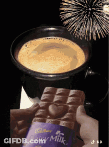 A Person Is Holding A Cadbury Dairy Milk Chocolate Bar In Front Of A Cup Of Coffee GIF