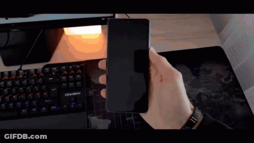 A Person Is Holding A Cell Phone In Front Of A Computer Keyboard GIF