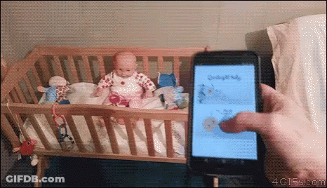 A Person Is Holding A Cell Phone In Front Of A Crib With A Baby In It .. GIF
