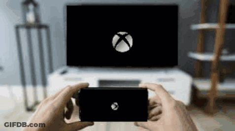 A Person Is Holding A Cell Phone In Front Of An Xbox Logo On A Television . GIF
