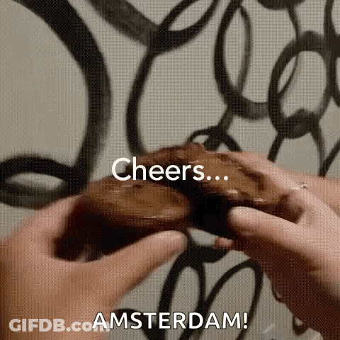 A Person Is Holding A Chocolate Donut In Their Hands With The Words `` Cheers Amsterdam '' Written On It . GIF
