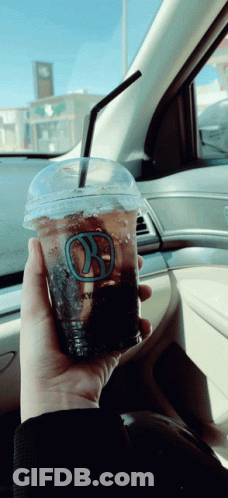 A Person Is Holding A Cup Of Coffee With A Straw In A Car GIF