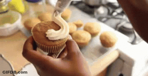 A Person Is Holding A Cupcake With Frosting On It In Their Hand . GIF