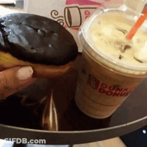 A Person Is Holding A Donut Next To A Dunkin Donuts Cup Of Coffee GIF
