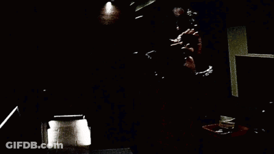 A Person Is Holding A Fan In Front Of A Couch In A Dark Room . GIF