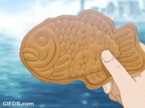 A Person Is Holding A Fish Shaped Biscuit In Their Hand . GIF