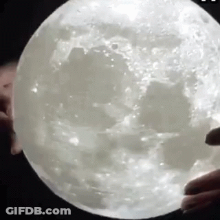 A Person Is Holding A Giant Moon In Their Hands . GIF