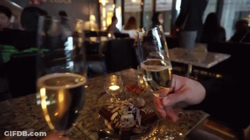 A Person Is Holding A Glass Of Champagne In Front Of A Dessert GIF