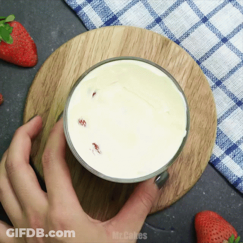 A Person Is Holding A Glass Of Milk On A Wooden Cutting Board With The Words Mr. Cakes Written On The Bottom GIF