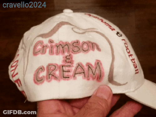 A Person Is Holding A Hat That Says Crimson And Cream GIF