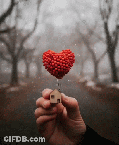 A Person Is Holding A Heart Shaped Balloon And A Small Wooden House GIF