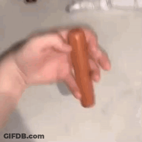 A Person Is Holding A Hot Dog In Their Hand On A Counter . GIF