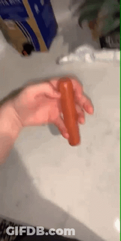 A Person Is Holding A Hot Dog In Their Hand On A Table . GIF