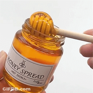 A Person Is Holding A Jar Of Honey Spread With A Honey Dipper In It GIF