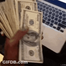 A Person Is Holding A Large Stack Of Money In Front Of A Laptop . GIF