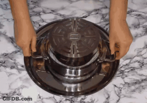 A Person Is Holding A Metal Tray With A Lid On Top Of It GIF