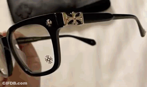 A Person Is Holding A Pair Of Glasses With A Cross On The Lenses . GIF