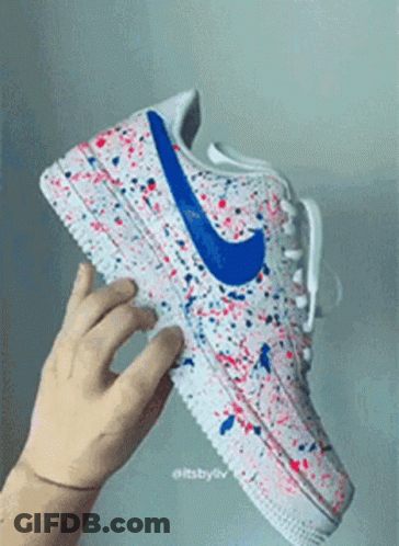 A Person Is Holding A Pair Of Nike Air Force 1 Sneakers With Red , White And Blue Paint Splatter On Them . GIF