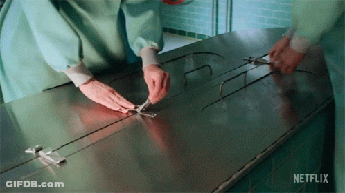 A Person Is Holding A Pair Of Scissors Over A Stainless Steel Table That Says Netflix On It . GIF
