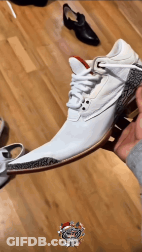A Person Is Holding A Pair Of White Shoes On A Wooden Floor With The Word Castro On The Bottom Right GIF