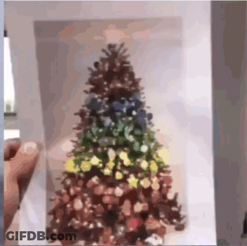 A Person Is Holding A Picture Of A Christmas Tree On A Piece Of Paper GIF
