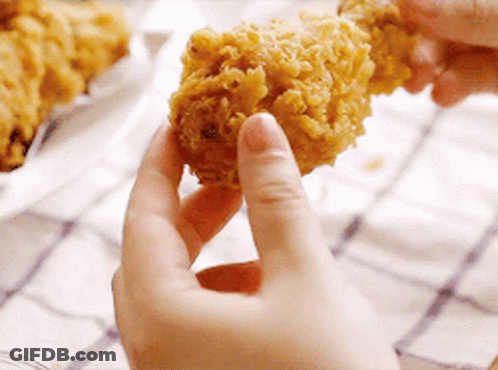 A Person Is Holding A Piece Of Fried Chicken Between Their Fingers . GIF