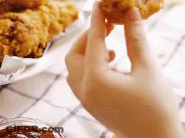 A Person Is Holding A Piece Of Fried Chicken . GIF