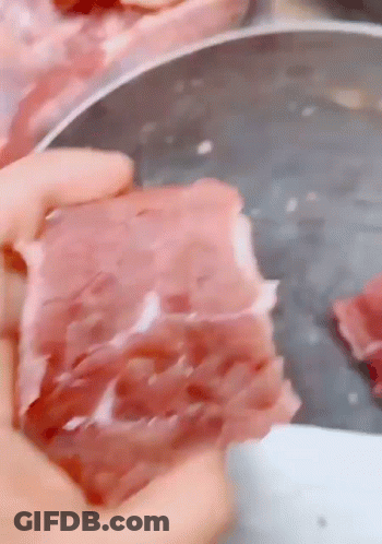 A Person Is Holding A Piece Of Raw Meat In Their Hand In Front Of A Cutting Board . GIF