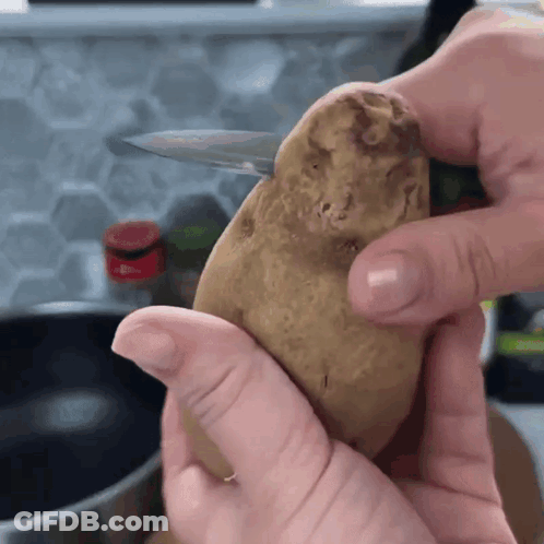 A Person Is Holding A Potato In Their Hands With A Knife In It GIF