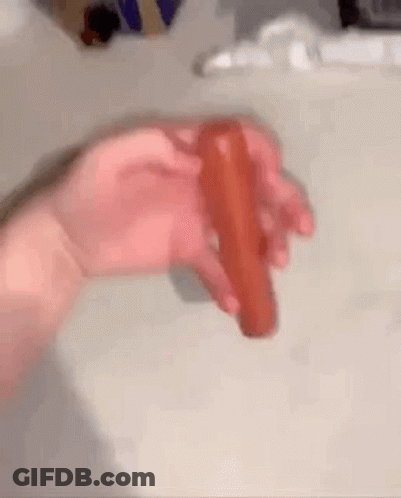A Person Is Holding A Red Hot Dog In Their Hand . GIF
