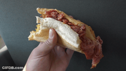 A Person Is Holding A Sandwich In Their Hand With A Bite Taken Out Of It GIF