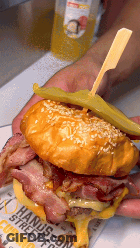 A Person Is Holding A Sandwich With A Pickle On A Newspaper That Says " Hands-On " GIF