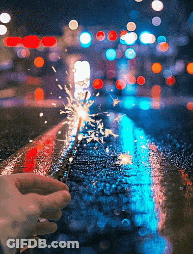 A Person Is Holding A Sparkler In Front Of A Blurry Background GIF