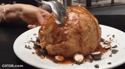 A Person Is Holding A Spoon Over A Dessert On A Plate . GIF