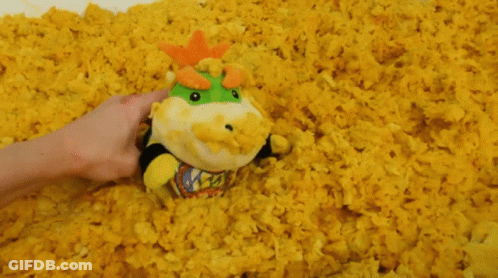 A Person Is Holding A Stuffed Animal In A Pile Of Yellow Popcorn GIF