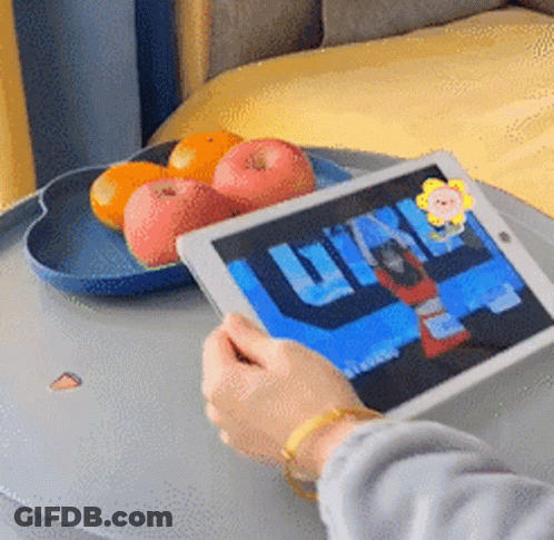 A Person Is Holding A Tablet In Front Of A Tray Of Apples And Oranges GIF