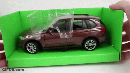 A Person Is Holding A Toy Car In A Green Box With The Door Open GIF
